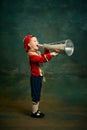 Little preschool age boy dressed up as medieval little prince and pageboy shouting at megaphone over dark vintage style