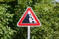 attention falling rocks traffic sign in front of green trees. caution, drive carefully. daytime sunshine without people Royalty Free Stock Photo