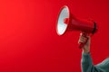 Attention grabbing image Hand holds megaphone against red background Royalty Free Stock Photo