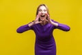 Attention! Portrait of aggressive woman holding her hands near wide open mouth. isolated on yellow background Royalty Free Stock Photo