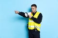 Portrait of young policeman officer wearing black uniform and warnvest shouting at megaphone isolated on blue background