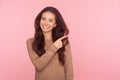 Attention to advertising! Portrait of cheerful young woman with brunette wavy hair pointing aside, showing copy space