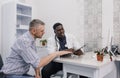 an attentive African-American doctor advises a patient during an appointment sitting at a table in a medical office.