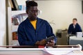 Attentive African American male in a blue uniform using calculator in the printing house