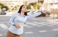 Attentive arab young woman in blue shirt hails taxi on city street, her focus intent