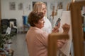 Concentrated aged woman standing in front of easel