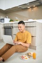 Attentive asian man using laptop while sitting on floor in kitchen Royalty Free Stock Photo