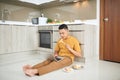 Attentive asian man using laptop while sitting on floor in kitchen Royalty Free Stock Photo