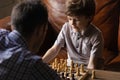 Attentive boy junior pupil playing chess with young male coach