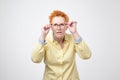 Attentive caucasian woman with short red hair looks scrupulously into distance, keeps hand on rim of spectacles. Royalty Free Stock Photo