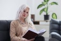 Attentive elderly woman reads book sitting in armchair Royalty Free Stock Photo