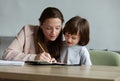 Attentive, funny toddler child diligently learning how to write and draw with his caring mother at home.