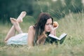 Attentive girl with apple lying on the green grass and reading a book.