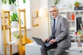 Attentive good-looking tidy man in grey outfit sitting on the edge of the table