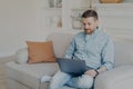 Attentive handsome young man in casual clothes using laptop while sitting on sofa Royalty Free Stock Photo