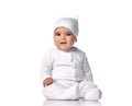 Attentive infant baby toddler in white jumpsuit overall and funny hat sits on the floor listens and tries to understand