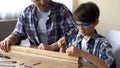 Attentive little boy hammering nail in wooden plank, father supporting his kid Royalty Free Stock Photo