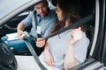 Attentive male driving instructor with badge on his neck shows female student how to fasten her belt. Attractive young Royalty Free Stock Photo