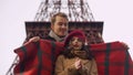 Attentive man wrapping his frozen beloved lady in blanket, openair date in Paris