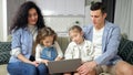 Attentive parents watch excited siblings playing on laptop