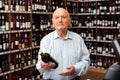 Attentive pensioner chooses red wine in a liquor store