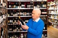 Attentive pensioner chooses red wine in a liquor store