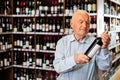 Attentive pensioner chooses red wine in a liquor store