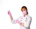 Red-haired lady doctor in medical coat, mask and gloves looking at camera showing aside warning about something important Royalty Free Stock Photo