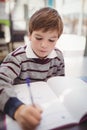 Attentive schoolboy writing in book in classroom