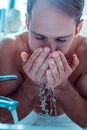 Attentive short-haired man wetting face in a sink