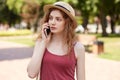 Attentive slender beautiful girl walking along park street, holding her smartphone near ear, talking over mobile phone, having Royalty Free Stock Photo