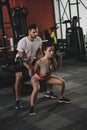 attentive trainer supporting young sportswoman lifting