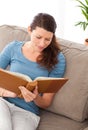 Attentive woman reading a book sitting on her sofa