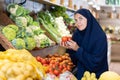 Attentive young Muslim woman purchaser choosing tomatoes in grocery store