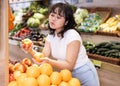 Attentive young woman purchaser choosing apples in grocery store