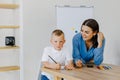 Attentive young woman tutor teacher helping little boy pupil with studying, correct mistakes explain learning material. Smiling