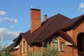 attic of a red brick house with windows under a brown tiled roof and a large chimney