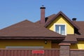 The attic of a yellow house with a white window under a brown tiled roof behind a fence Royalty Free Stock Photo