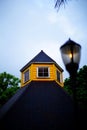 attic of a yellow house with white windows under a green tiled roof against the sky