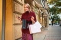Attractice excited styliah blond girl thoughtfully looking in shopping bag on street