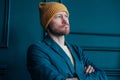 Attractive adult bearded angry man hipster in yellow hat looks at camera and furrowed his brows on blue wall background