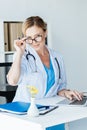 attractive adult female doctor in eyeglasses looking at camera while working on laptop at table Royalty Free Stock Photo