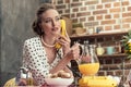 attractive adult housewife holding jug of orange juice talking by vintage wired phone Royalty Free Stock Photo