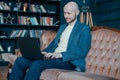 Attractive adult successful smiling bald man with beard in suit working at laptop on his rich cabinet Royalty Free Stock Photo