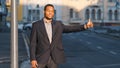 Attractive African American student, young guy in suit waiting for cab outdoors. Modern businessman or manager gesturing Royalty Free Stock Photo