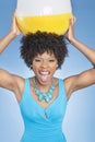 Attractive African American woman holding beach ball aloft over colored background Royalty Free Stock Photo