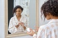 Attractive african american woman looking in mirror and apply facial cream Royalty Free Stock Photo