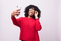 Attractive african woman with afro taking a picture of herself with her camera phone isolated on white background Royalty Free Stock Photo