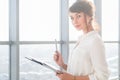 Attractive ambitious businesswoman standing in modern office, holding paper folder, looking at camera, smiling. Royalty Free Stock Photo