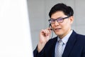 Attractive Asian Businessman work with phone, headset at call center and telemaketing sale support workplace. Customer service